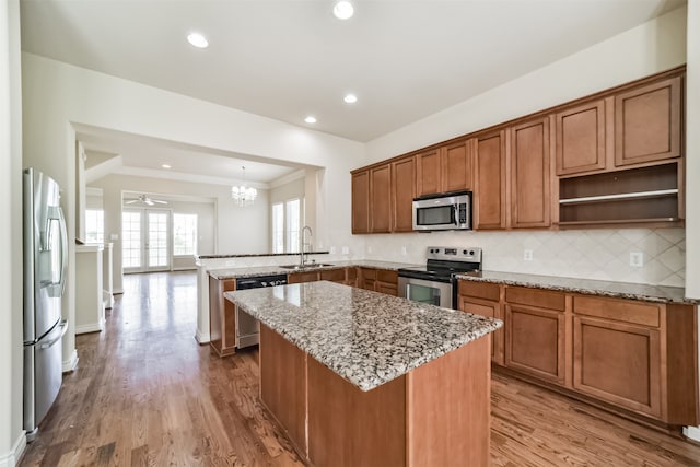 kitchen with light wood-type flooring, ceiling fan with notable chandelier, appliances with stainless steel finishes, sink, and kitchen peninsula