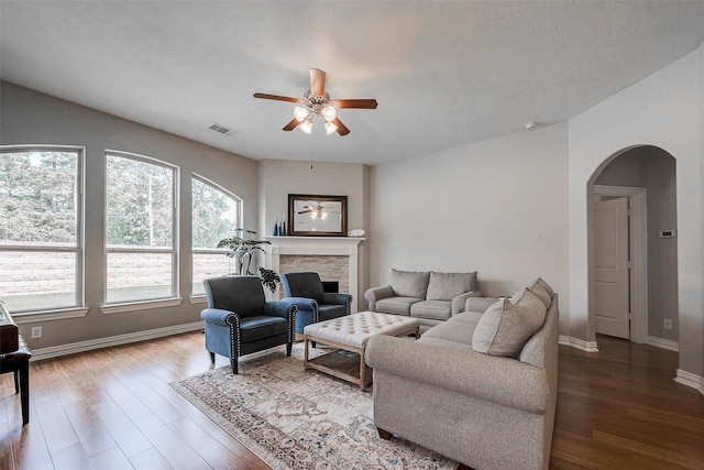 living area with a stone fireplace, visible vents, wood finished floors, and arched walkways