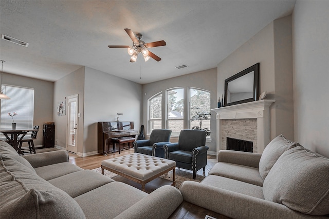 living room featuring a fireplace, a textured ceiling, light hardwood / wood-style flooring, and ceiling fan