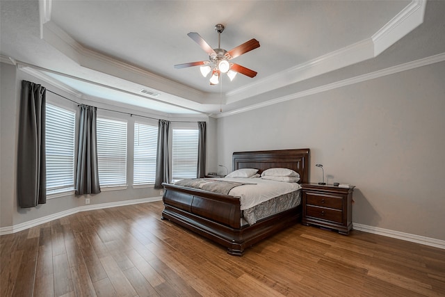 bedroom with a tray ceiling, ornamental molding, hardwood / wood-style flooring, and ceiling fan