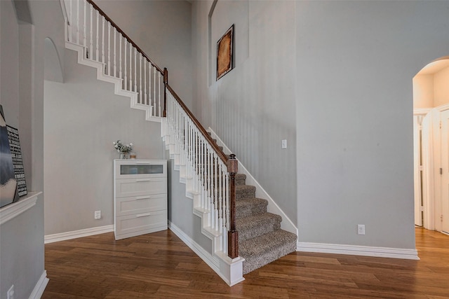 staircase featuring wood finished floors, arched walkways, a towering ceiling, and baseboards