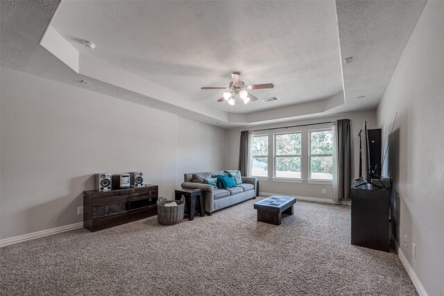 carpeted living room with a textured ceiling, a raised ceiling, and ceiling fan