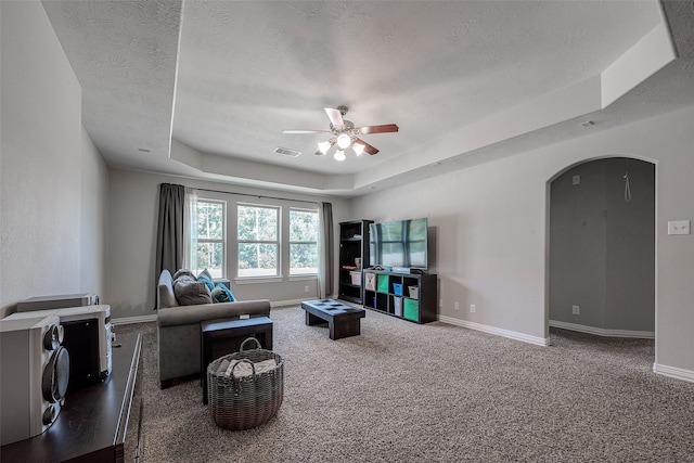 living room with ceiling fan, a raised ceiling, a textured ceiling, and carpet floors