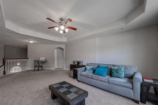 living area with baseboards, carpet, a tray ceiling, arched walkways, and a ceiling fan