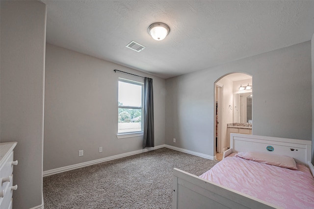 unfurnished bedroom with a textured ceiling, connected bathroom, and carpet floors