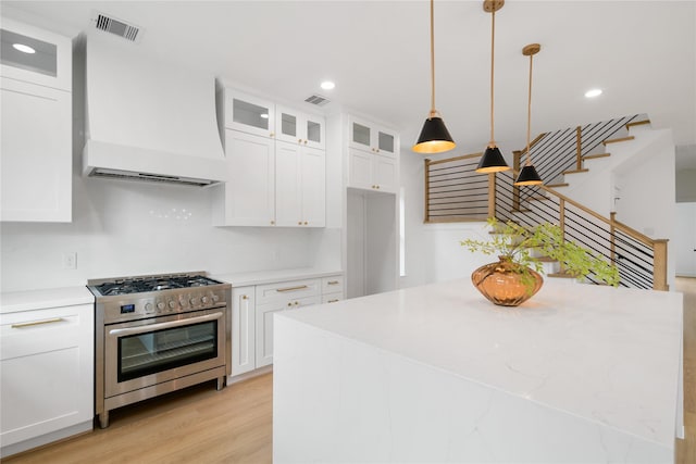 kitchen featuring premium range hood, stainless steel range with gas cooktop, white cabinets, and decorative light fixtures