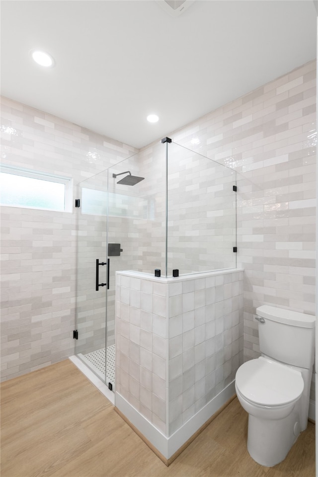 bathroom featuring tile walls, wood-type flooring, a shower with door, and toilet