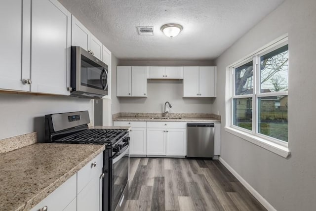 kitchen featuring wood-type flooring, sink, white cabinets, stainless steel appliances, and light stone countertops