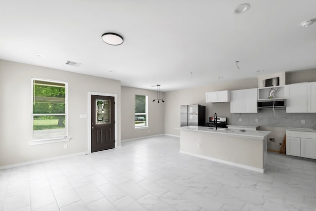 kitchen with white cabinets, hanging light fixtures, stainless steel refrigerator with ice dispenser, decorative backsplash, and a center island with sink