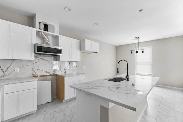 kitchen featuring a kitchen island with sink, decorative light fixtures, sink, and white cabinets