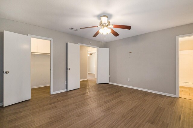 unfurnished bedroom featuring hardwood / wood-style flooring, a spacious closet, ceiling fan, and a closet