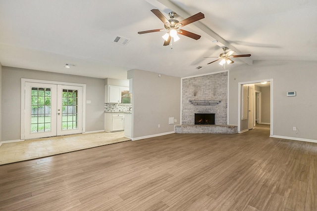 unfurnished living room featuring a large fireplace, light wood finished floors, visible vents, lofted ceiling with beams, and french doors