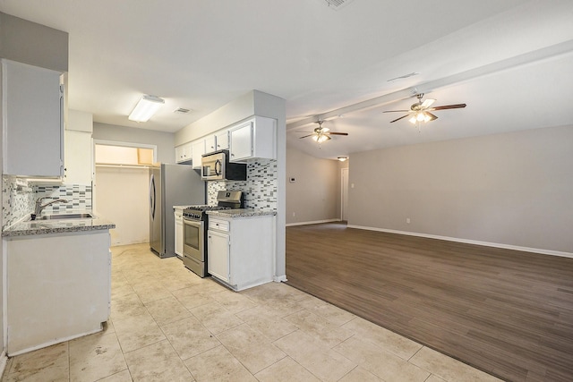 kitchen with decorative backsplash, appliances with stainless steel finishes, a sink, ceiling fan, and baseboards