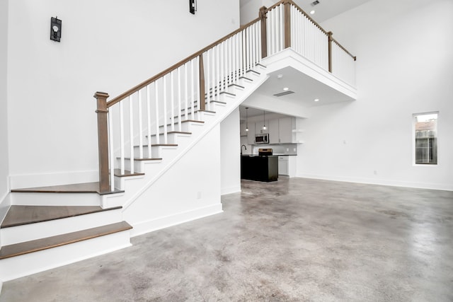 staircase featuring concrete flooring and a high ceiling