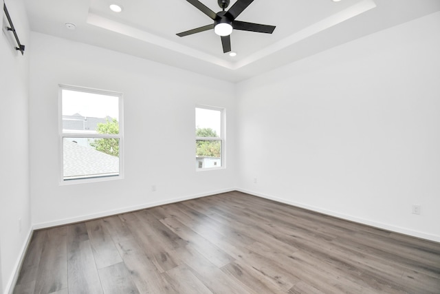 empty room with ceiling fan, light hardwood / wood-style flooring, and a tray ceiling