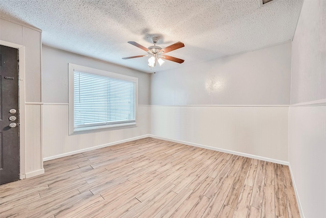 empty room with ceiling fan, a wainscoted wall, a textured ceiling, and wood finished floors