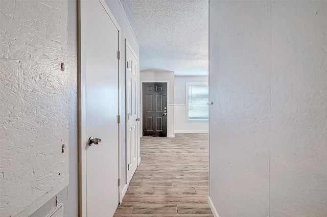 corridor with light hardwood / wood-style floors and a textured ceiling