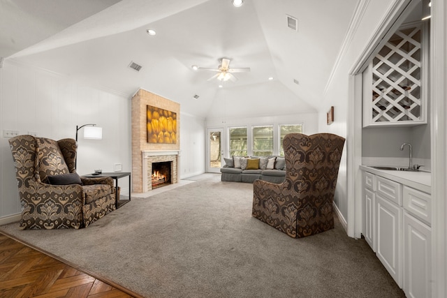 living room featuring lofted ceiling, ceiling fan, ornamental molding, a fireplace, and indoor wet bar