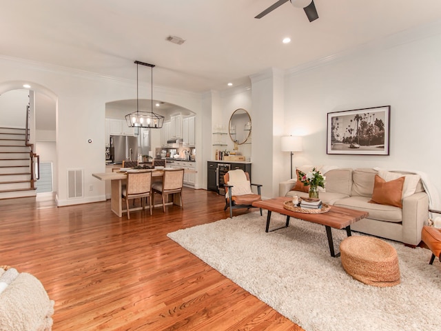 living room featuring ornamental molding, hardwood / wood-style floors, ceiling fan with notable chandelier, and wine cooler