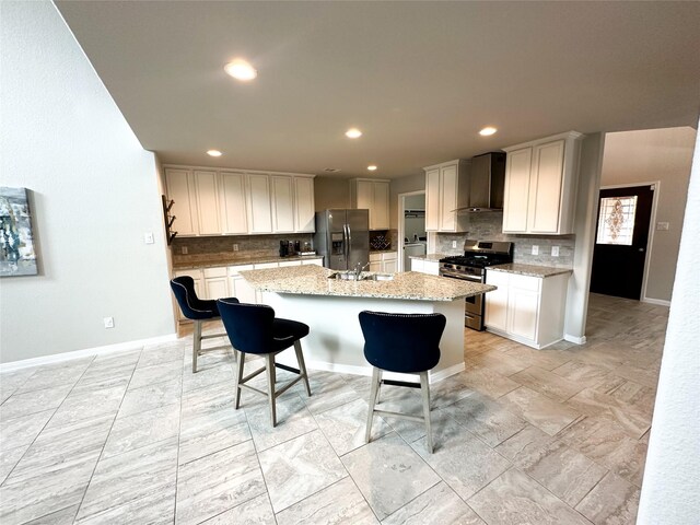 kitchen featuring a center island with sink, stainless steel appliances, light stone counters, and white cabinetry