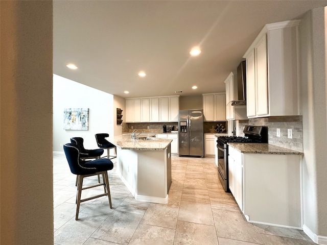 kitchen with white cabinetry, stainless steel appliances, light stone counters, decorative backsplash, and wall chimney range hood