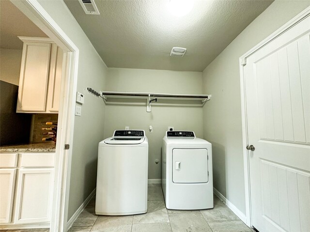 clothes washing area featuring a textured ceiling, cabinets, washer and clothes dryer, and light tile patterned floors