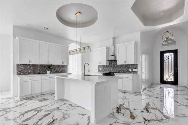 kitchen with a kitchen island with sink, pendant lighting, white cabinetry, tasteful backsplash, and wall chimney range hood