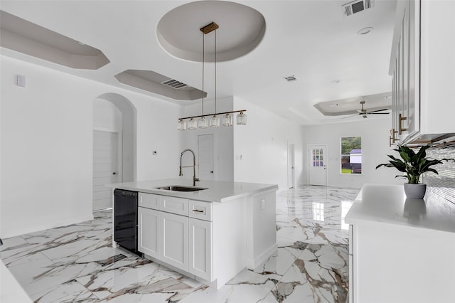 kitchen with a center island with sink, pendant lighting, sink, white cabinetry, and ceiling fan