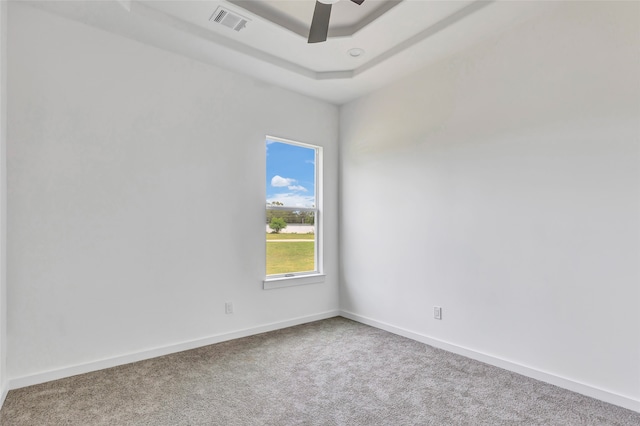 carpeted empty room with ceiling fan and a raised ceiling