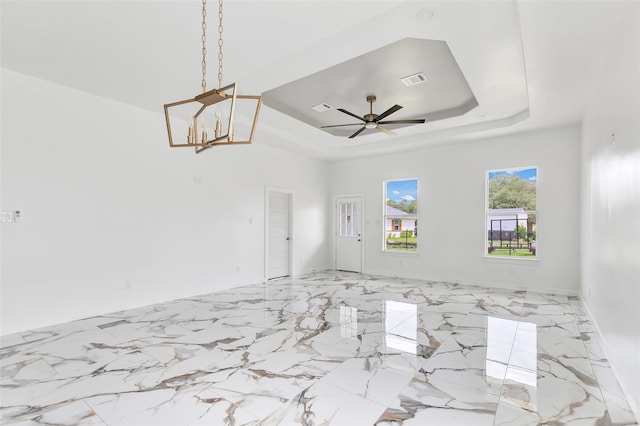 spare room with ceiling fan with notable chandelier and a raised ceiling