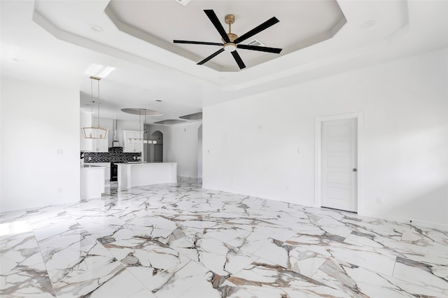 unfurnished living room featuring a raised ceiling and ceiling fan