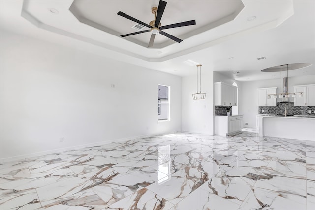 unfurnished living room featuring a raised ceiling, sink, and ceiling fan