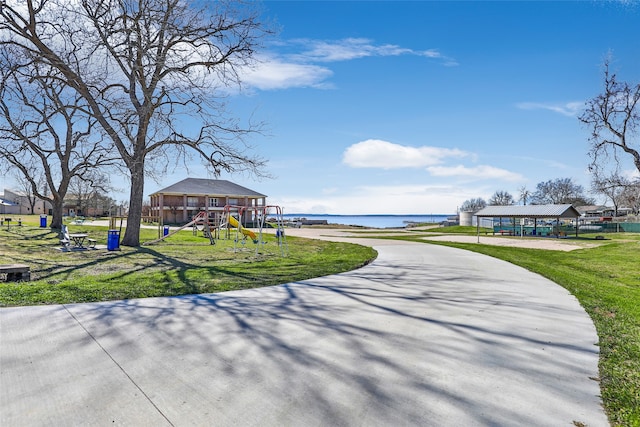 view of community featuring a water view, a lawn, and a playground