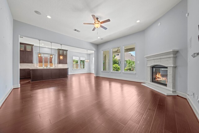 unfurnished living room featuring dark wood-type flooring, a textured ceiling, and ceiling fan