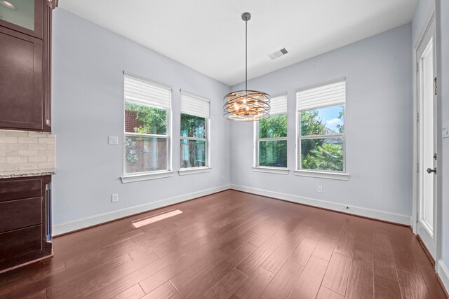 unfurnished dining area featuring a notable chandelier, plenty of natural light, and dark hardwood / wood-style floors