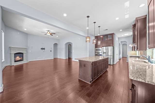 kitchen with light stone counters, a kitchen island, decorative light fixtures, stainless steel appliances, and dark hardwood / wood-style flooring