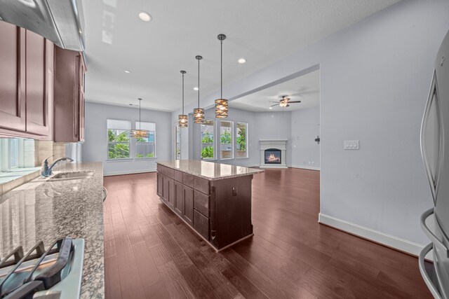 kitchen with sink, a kitchen island, decorative light fixtures, light stone countertops, and dark hardwood / wood-style flooring