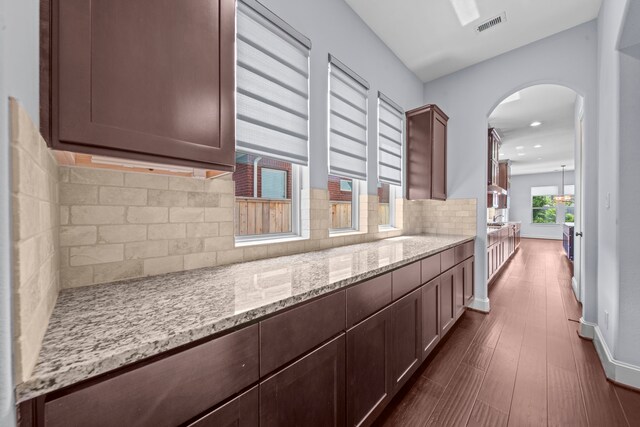 kitchen featuring dark brown cabinets, backsplash, light stone countertops, and dark hardwood / wood-style floors