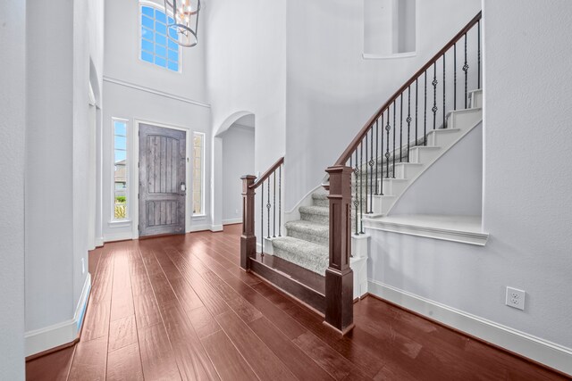 entryway with a notable chandelier, a towering ceiling, and wood-type flooring