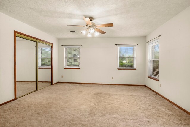 unfurnished bedroom featuring a closet, light colored carpet, ceiling fan, and a textured ceiling