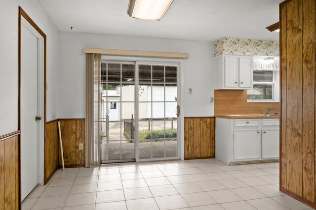 kitchen featuring light tile patterned floors, white cabinetry, and wood walls