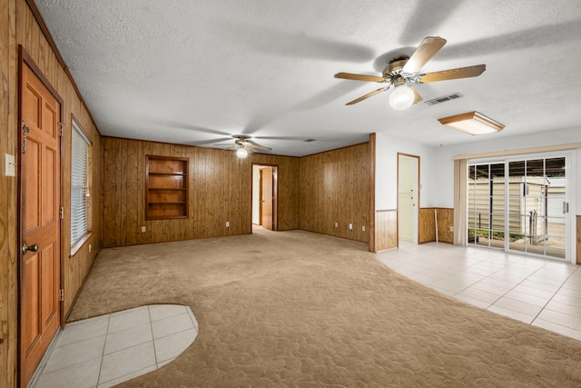 unfurnished room featuring a textured ceiling, light colored carpet, ceiling fan, and wood walls