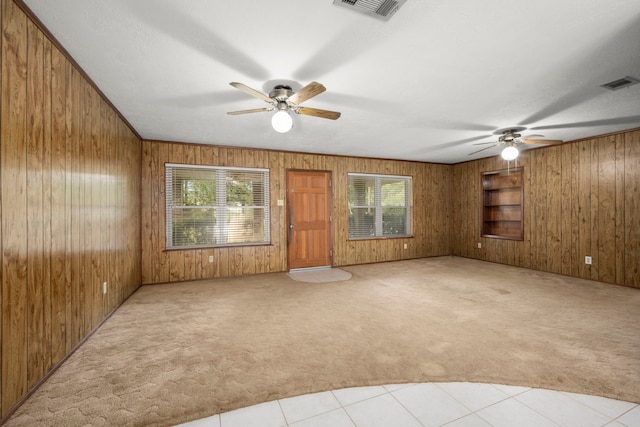 unfurnished living room featuring light carpet, plenty of natural light, ceiling fan, and wooden walls