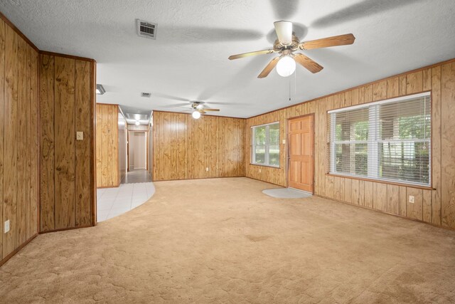 carpeted empty room with a textured ceiling, ceiling fan, and wooden walls