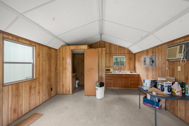 interior space with vaulted ceiling, a wall mounted air conditioner, sink, electric panel, and wooden walls