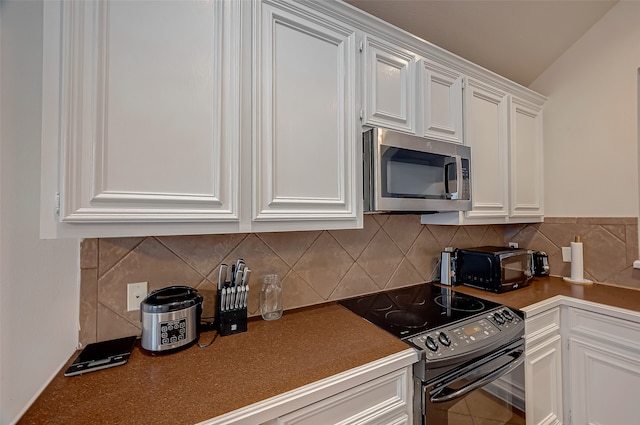 kitchen featuring black electric range, vaulted ceiling, white cabinetry, and tasteful backsplash