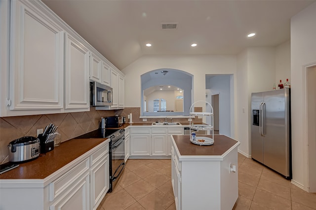 kitchen featuring light tile patterned floors, a center island, vaulted ceiling, stainless steel appliances, and white cabinetry