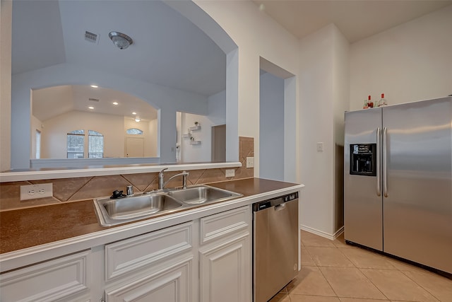 kitchen with vaulted ceiling, stainless steel appliances, white cabinetry, sink, and light tile patterned flooring