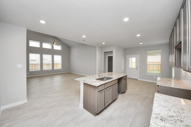 kitchen featuring light stone countertops, ceiling fan, a kitchen island with sink, sink, and light hardwood / wood-style flooring