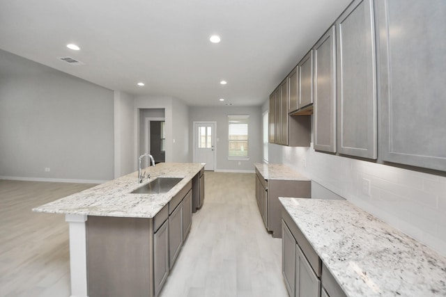 kitchen featuring decorative backsplash, light wood-type flooring, stainless steel dishwasher, sink, and a center island with sink